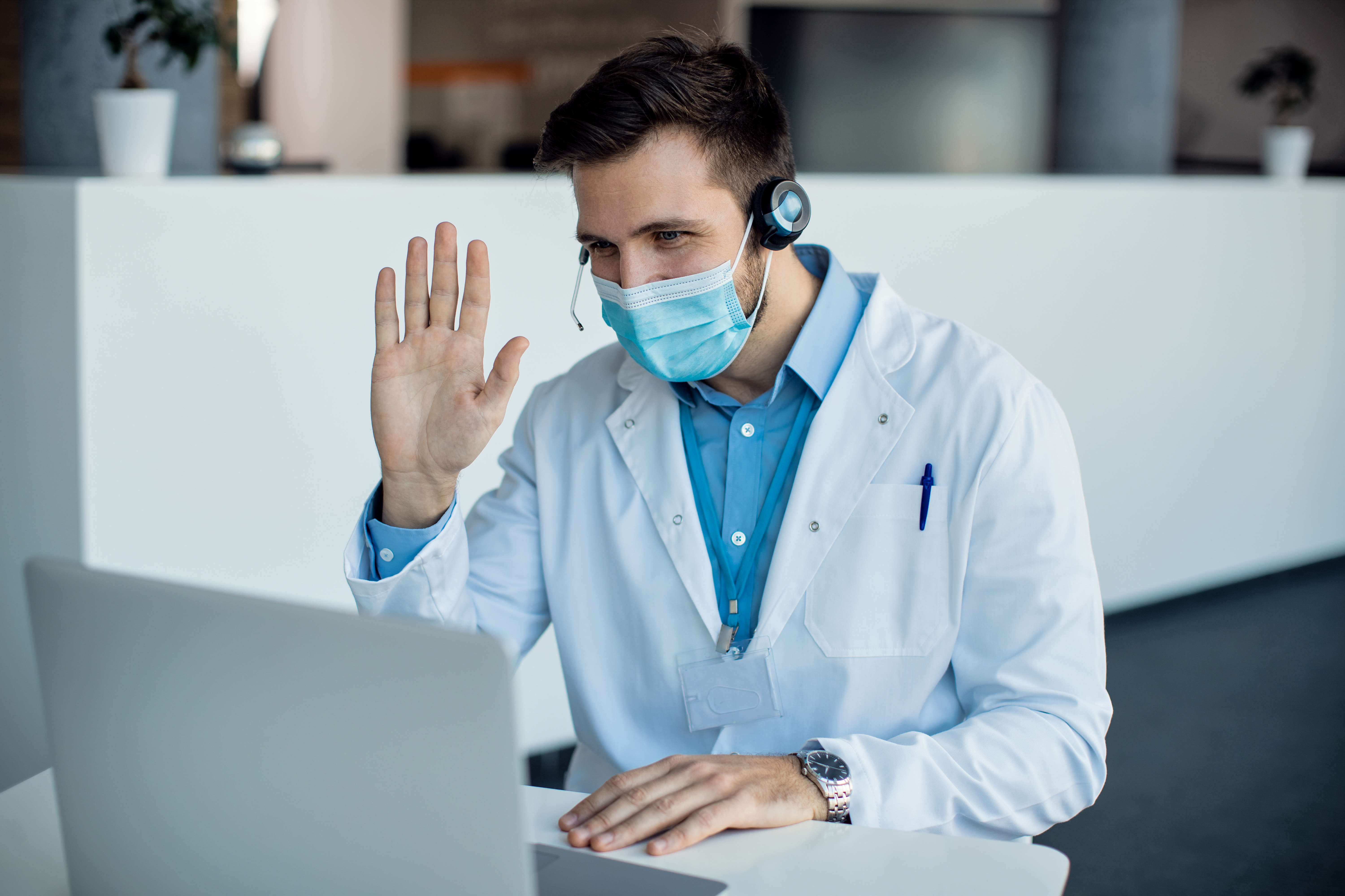 Male doctor waving during a video call over laptop at medical c